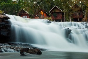 The serene Tad Lo waterfall surrounded by lush vegetation and traditional bungalows, located in the Bolaven Plateau which was named after the Laven ethnic group which has historically dominated the region.