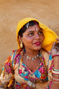 Portrait of a tribal woman wearing colourful clothing in front of a traditional mud walled house, located in a small village called Mool Sagar close to the famous Sam sand dunes.