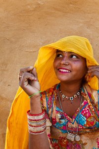 Portrait of a tribal woman wearing colourful clothing in front of a traditional mud walled house, located in a small village called Mool Sagar close to the famous Sam sand dunes.