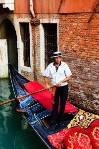 Gondolier taking tourists on gondola boat ride on the narrow canals of the UNESCO World Heritage Site of Venice.
